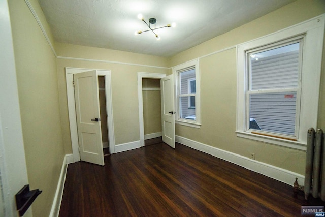 unfurnished bedroom featuring a chandelier, radiator heating unit, and dark wood-type flooring