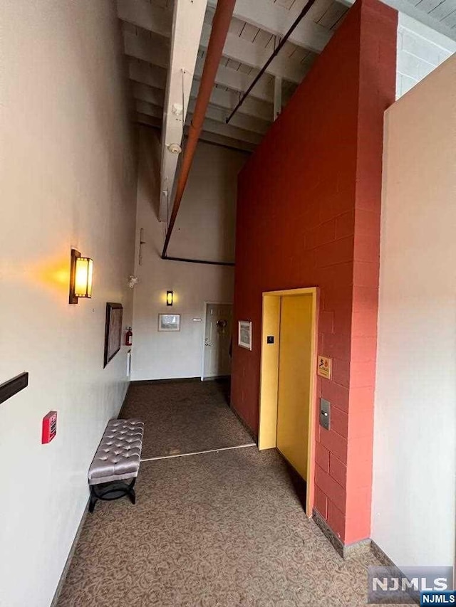 hallway featuring dark colored carpet, a towering ceiling, and elevator