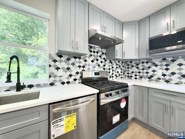 kitchen with sink, light hardwood / wood-style flooring, backsplash, stainless steel appliances, and light stone countertops