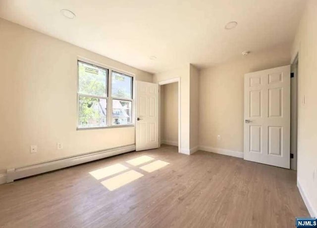 unfurnished bedroom with wood-type flooring and baseboard heating