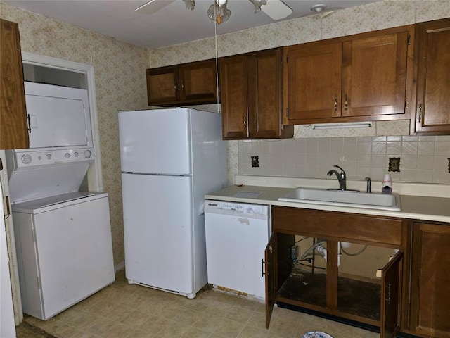 kitchen featuring white appliances, backsplash, sink, ceiling fan, and stacked washing maching and dryer