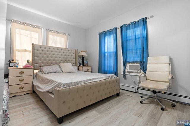 bedroom featuring light hardwood / wood-style floors, a baseboard radiator, and cooling unit