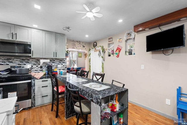 kitchen featuring a breakfast bar area, gray cabinets, light wood-type flooring, and appliances with stainless steel finishes