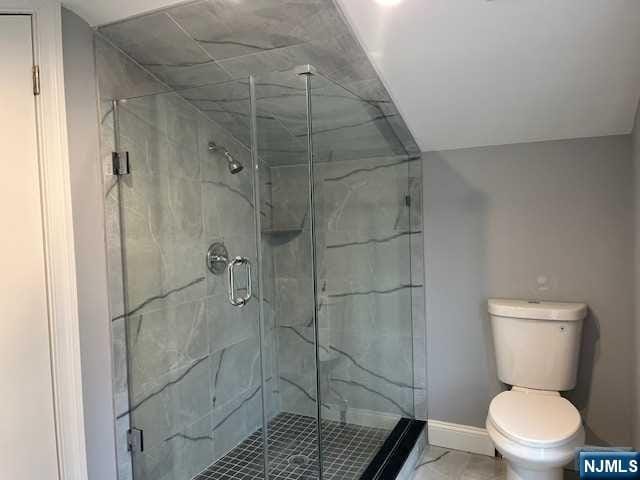 bathroom featuring a shower with door and toilet