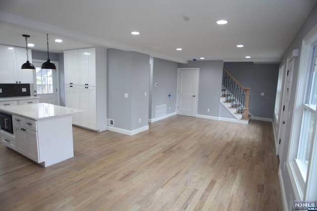 kitchen featuring backsplash, pendant lighting, white cabinets, a center island, and light hardwood / wood-style floors