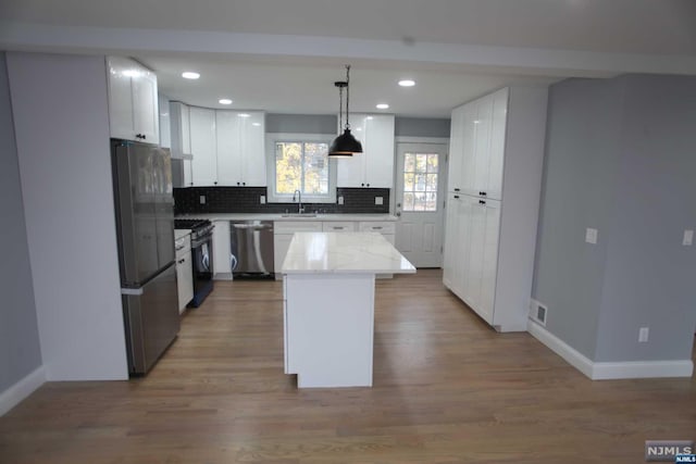 kitchen with sink, hanging light fixtures, stainless steel appliances, a kitchen island, and white cabinets