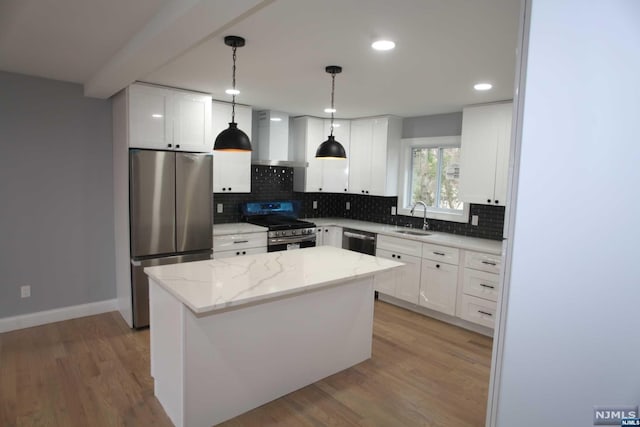 kitchen featuring appliances with stainless steel finishes, wall chimney exhaust hood, sink, white cabinets, and a kitchen island