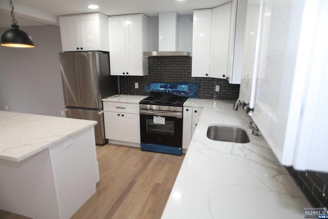 kitchen featuring appliances with stainless steel finishes, white cabinetry, pendant lighting, and wall chimney range hood