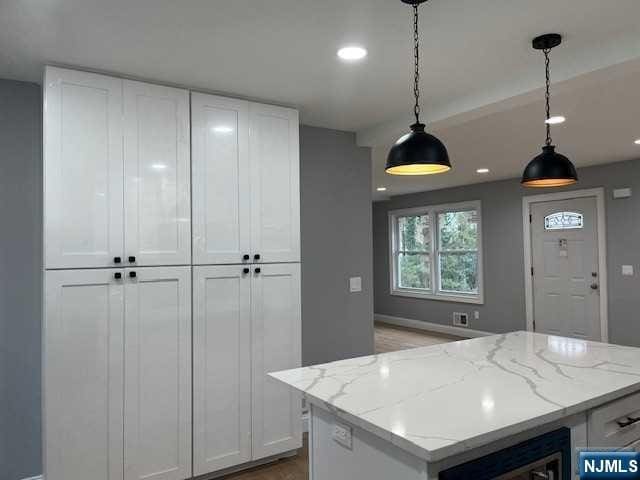 kitchen with white cabinetry, pendant lighting, a center island, and light stone countertops