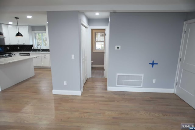 kitchen with tasteful backsplash, sink, pendant lighting, light hardwood / wood-style flooring, and white cabinetry