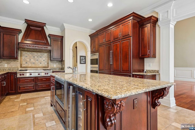 kitchen with stainless steel appliances, wine cooler, an island with sink, a breakfast bar, and custom range hood