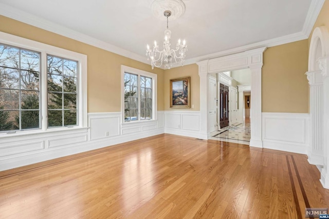 unfurnished dining area with ornate columns, light wood-type flooring, ornamental molding, and an inviting chandelier