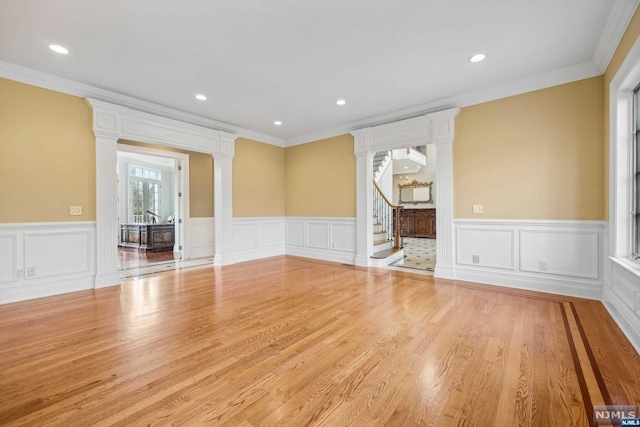 spare room featuring ornate columns, ornamental molding, and light hardwood / wood-style flooring