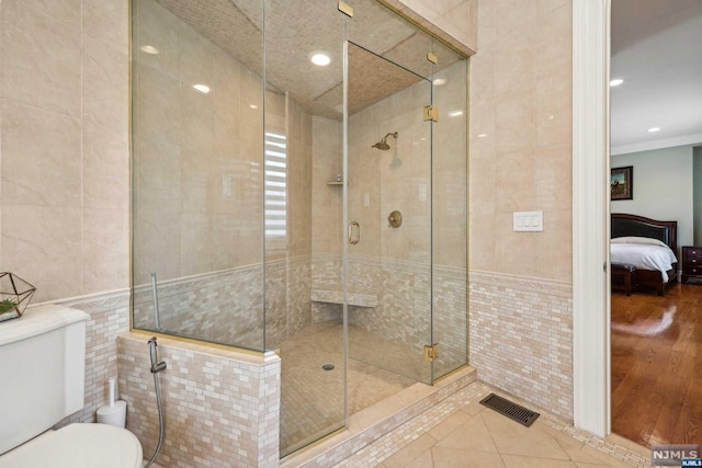 bathroom featuring an enclosed shower, ornamental molding, wood-type flooring, tile walls, and toilet