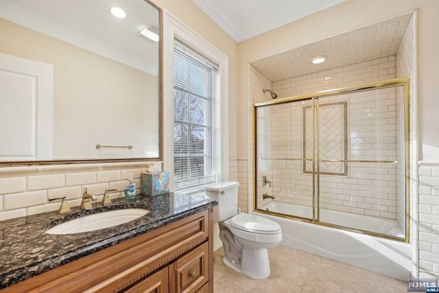 full bathroom featuring vanity, bath / shower combo with glass door, toilet, ornamental molding, and tile walls