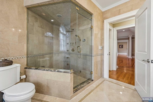 bathroom with hardwood / wood-style floors, toilet, a shower with shower door, tile walls, and ornamental molding