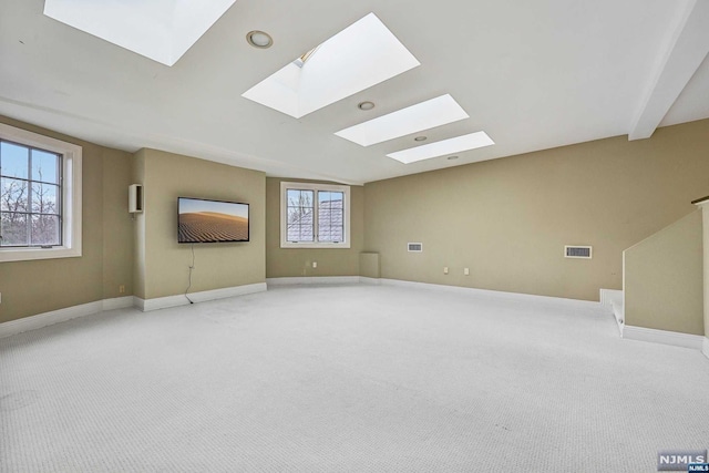 carpeted empty room with plenty of natural light, beam ceiling, and a skylight