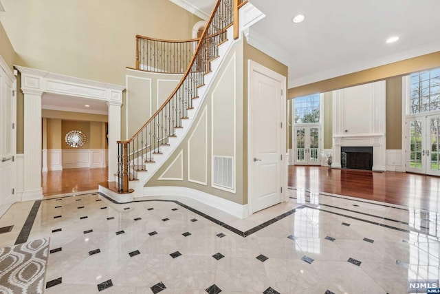 entrance foyer featuring ornate columns, crown molding, a towering ceiling, and french doors