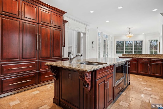 kitchen featuring stainless steel microwave, sink, light stone counters, pendant lighting, and a center island with sink