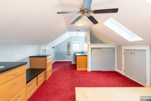 bonus room with dark colored carpet, lofted ceiling with skylight, and ceiling fan