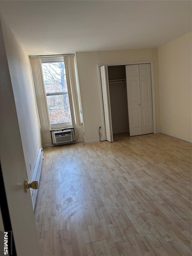 unfurnished bedroom with a wall mounted air conditioner, light hardwood / wood-style flooring, and baseboard heating