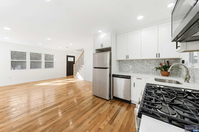 kitchen featuring white cabinetry, sink, decorative backsplash, appliances with stainless steel finishes, and light wood-type flooring