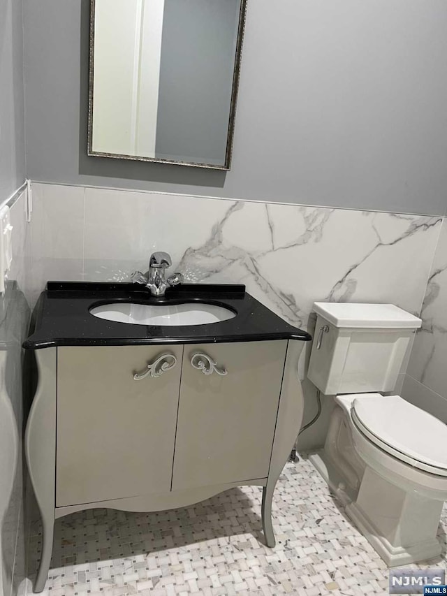 bathroom with vanity, toilet, and tile walls