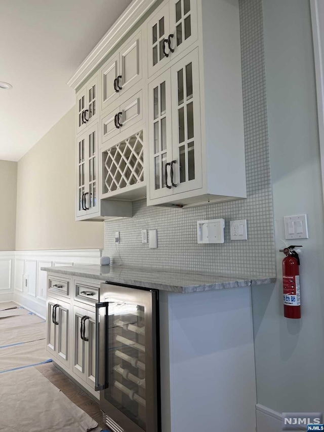 kitchen featuring white cabinetry, light stone countertops, tasteful backsplash, wine cooler, and light wood-type flooring