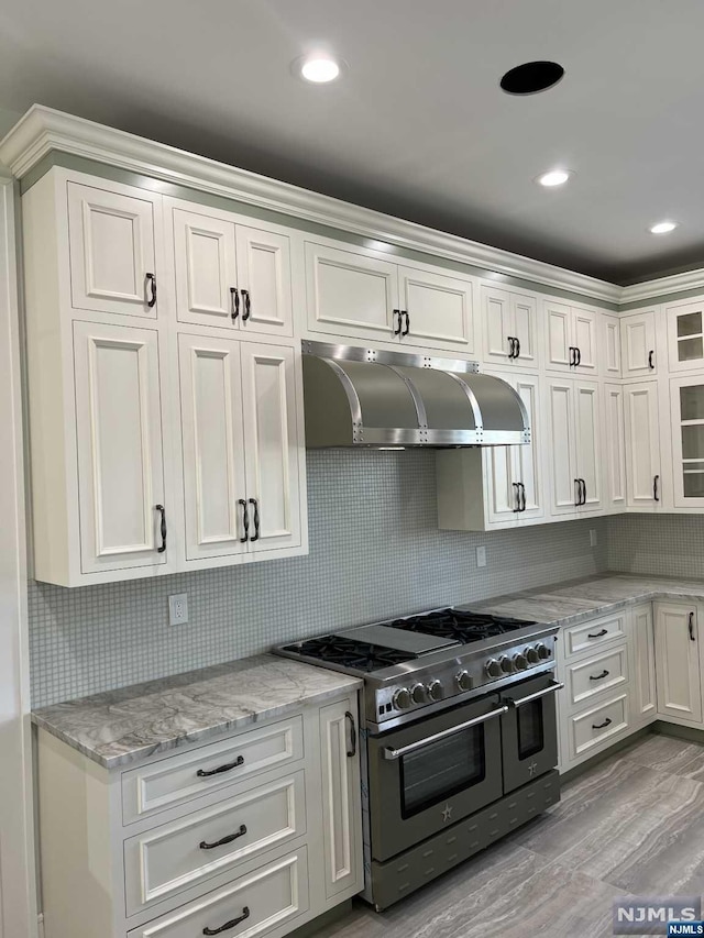 kitchen featuring light stone counters, range hood, double oven range, light hardwood / wood-style floors, and white cabinets