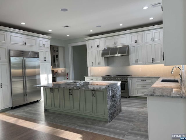 kitchen featuring high quality appliances, sink, a kitchen island, and light stone counters