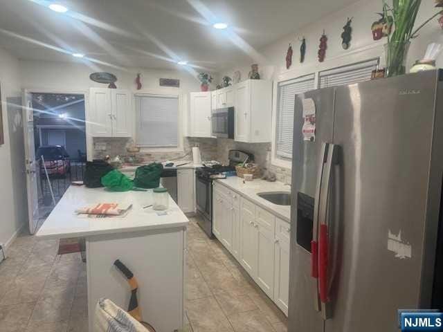 kitchen with backsplash, white cabinets, sink, appliances with stainless steel finishes, and a kitchen island