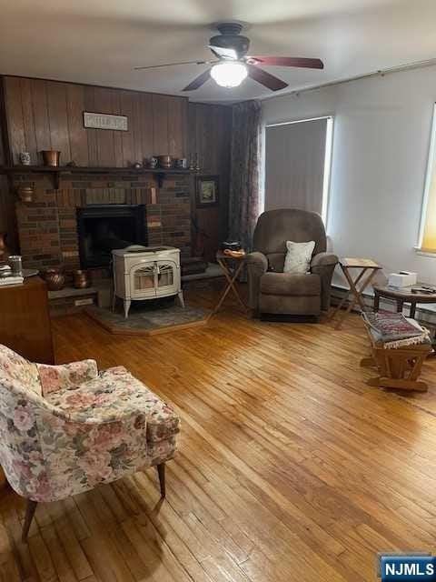 living room with light hardwood / wood-style flooring, a wood stove, ceiling fan, and wood walls