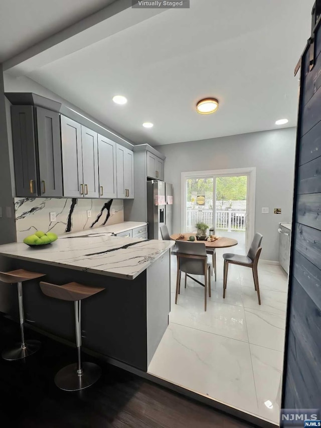 kitchen with light stone countertops, stainless steel fridge, tasteful backsplash, a barn door, and gray cabinets