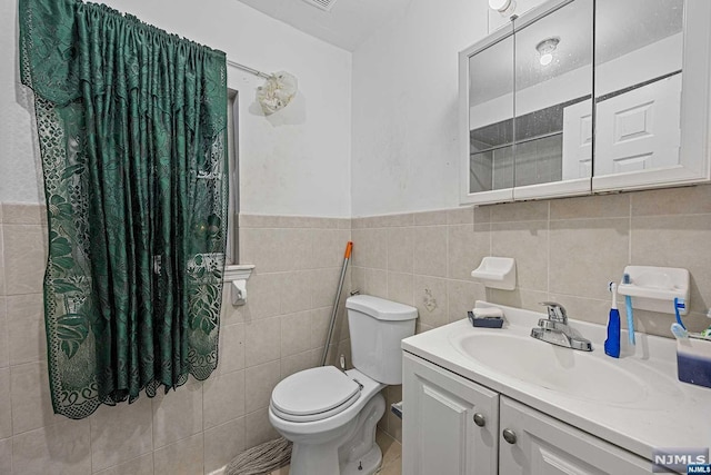 bathroom with vanity, toilet, and tile walls