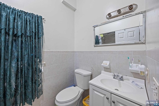 bathroom with vanity, toilet, and tile walls