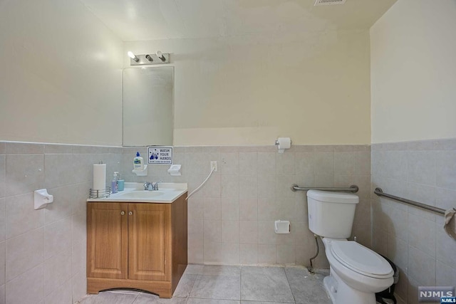 bathroom with toilet, vanity, tile patterned floors, and tile walls