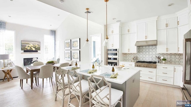 kitchen with a breakfast bar, white cabinetry, hanging light fixtures, a center island with sink, and stainless steel appliances