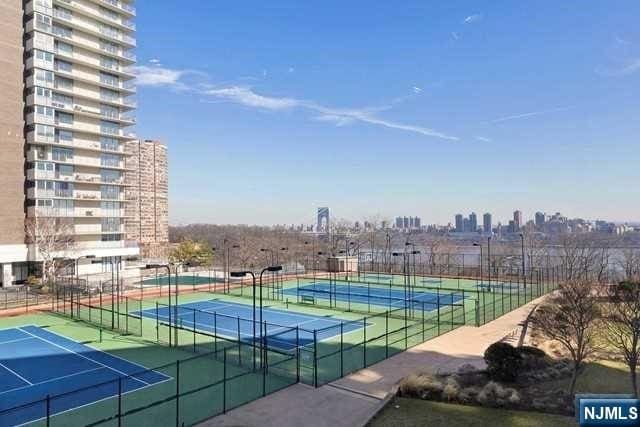 view of tennis court with a view of city and fence