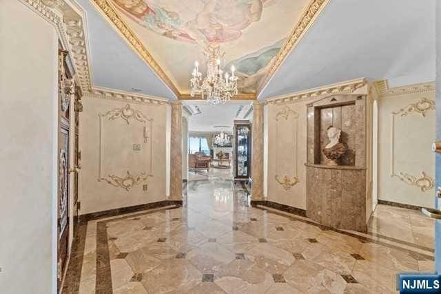 corridor with ornate columns, a tray ceiling, ornamental molding, and an inviting chandelier