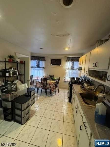 kitchen with light tile patterned flooring, white cabinetry, black appliances, and sink