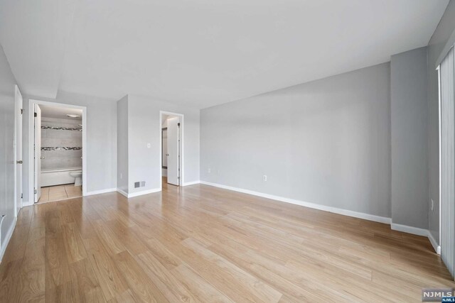 unfurnished bedroom featuring ensuite bathroom, a closet, a walk in closet, and light hardwood / wood-style flooring