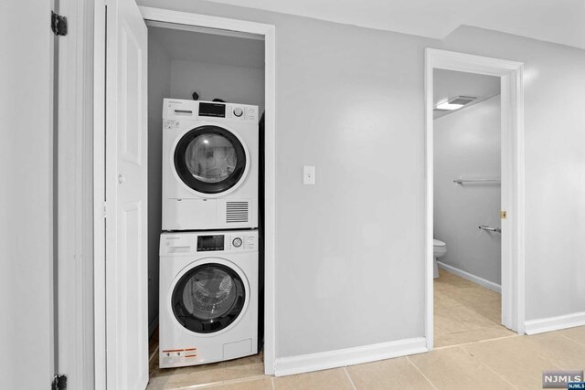 clothes washing area featuring light tile patterned floors and stacked washer and dryer