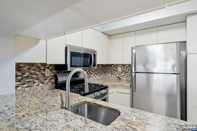 kitchen featuring white cabinetry, sink, stainless steel appliances, light stone counters, and decorative backsplash