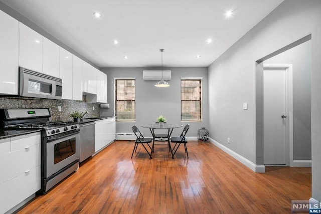 kitchen with stainless steel appliances, a wall unit AC, hardwood / wood-style floors, white cabinetry, and hanging light fixtures