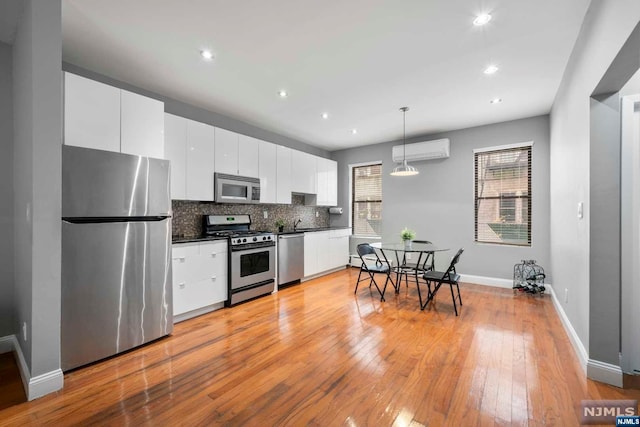 kitchen with pendant lighting, an AC wall unit, light hardwood / wood-style flooring, white cabinetry, and stainless steel appliances