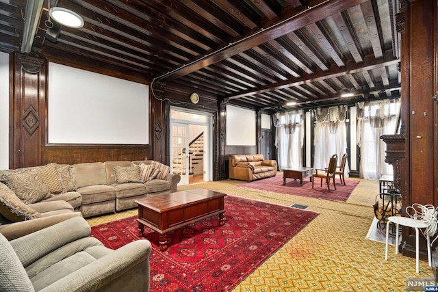 carpeted living room with beam ceiling and wooden walls