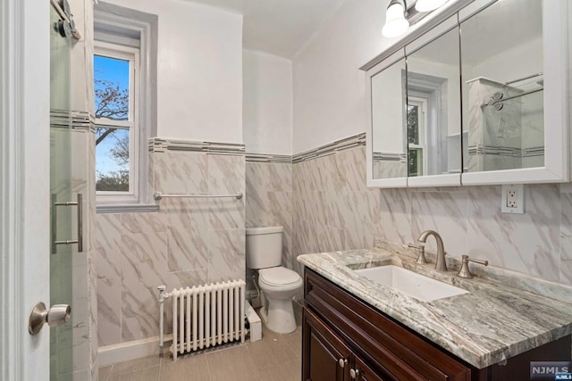 bathroom featuring vanity, toilet, radiator heating unit, and tile walls