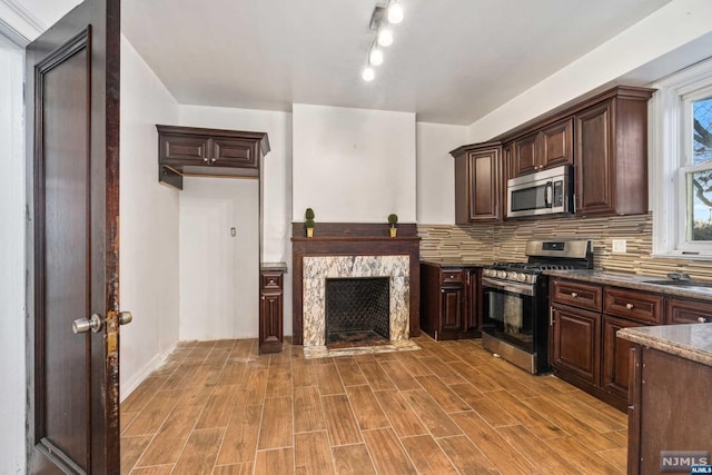 kitchen featuring tasteful backsplash, light hardwood / wood-style flooring, a high end fireplace, dark stone countertops, and appliances with stainless steel finishes