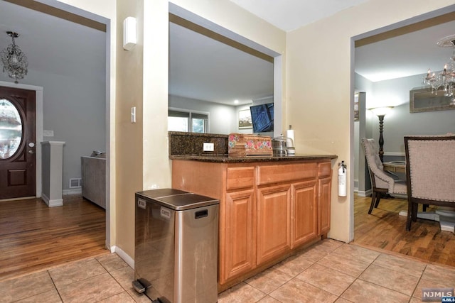 kitchen with dark stone countertops, tasteful backsplash, decorative light fixtures, light hardwood / wood-style floors, and stainless steel refrigerator