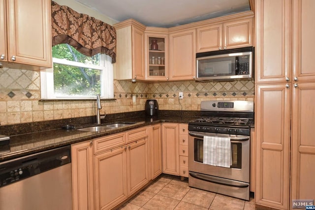 kitchen with backsplash, dark stone counters, sink, light tile patterned floors, and appliances with stainless steel finishes